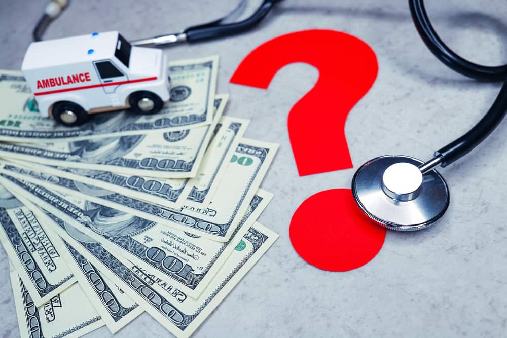 A toy ambulance and stethoscope sit atop 100-dollar bills to stress how a reference-based pricing model could mean significant savings for your company.