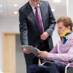 A patient sits in a wheelchair discussing cost containment in healthcare.