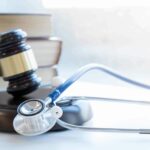 A stethoscope lays atop a gavel on a white desk to visualize how the payment integrity information act of 2019 impacts healthcare