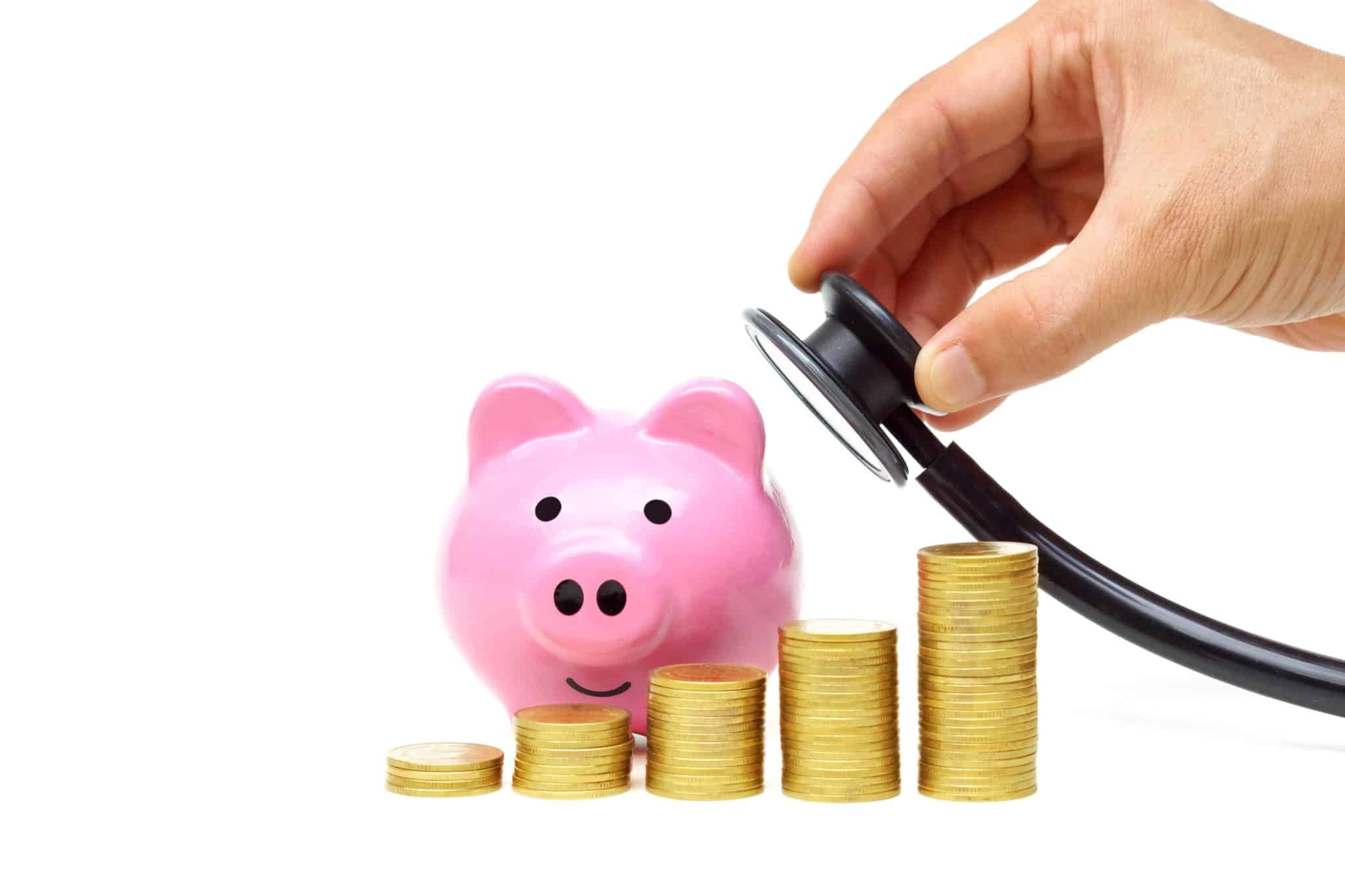 A doctor holds a stethoscope to a piggy bank behind stacks of coins to show potential savings from understanding pros and cons of managed care